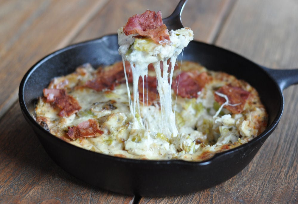 Heißer Käse-Dip mit Rosenkohl und Speckstreifen in Gusseisen-Pfanne, mit verschmolzenem Käse auf Servierlöffel