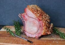 Gegrillter Kotelettbraten vom Schwarzwälder Kräuterschwein mit Kräuterkruste auf Holzbrett, garniert mit Rosmarin und Fleur de Sel