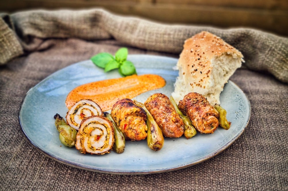 Griechische Schnitzelröllchen vom Drehspieß auf blauem Teller mit gegrillten Paprikaschoten, Pitabrot und frischem Basilikum