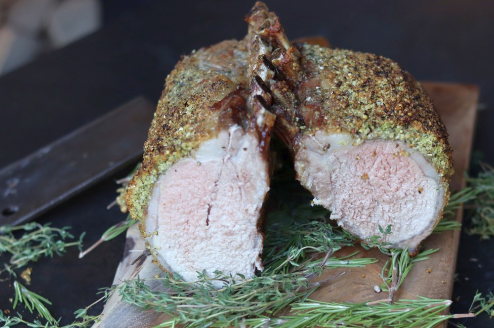 Iberico-Karree mit Parmesan-Kräuterkruste, aufgeschnitten auf Holzbrett mit Rosmarin, zartes rosa Fleischinneres sichtbar