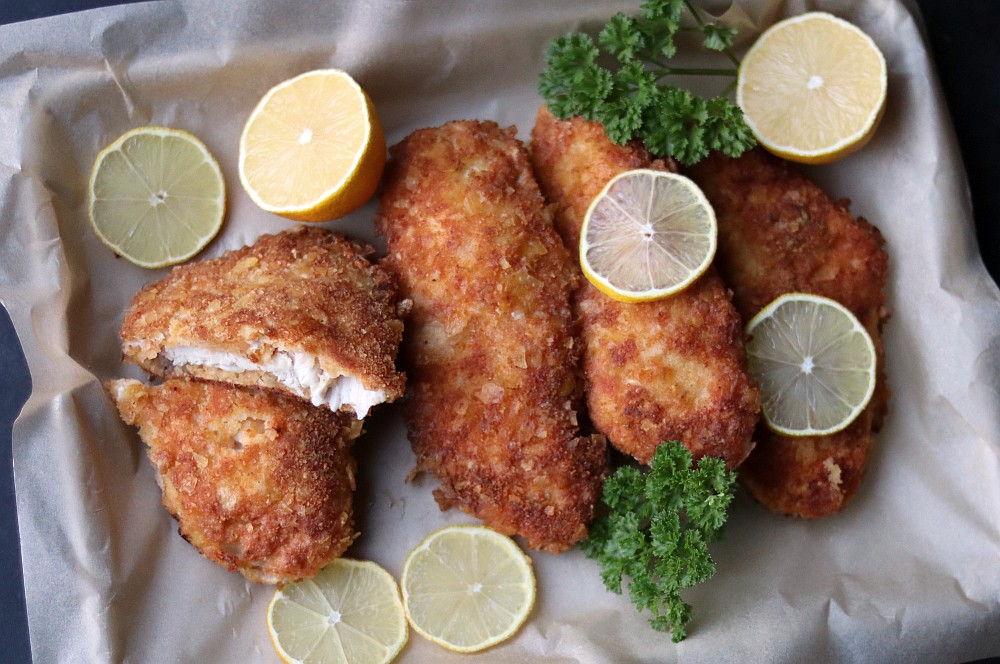 Knusprig frittierte Hähnchenschnitzel mit Chipskruste auf Backpapier, garniert mit Zitronenscheiben und Petersilie