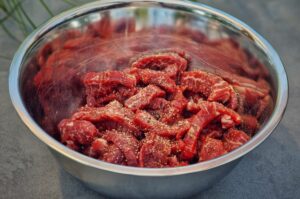 Gewürzte Rindfleischschnipsel in einer Edelstahlschüssel für Mongolisches Rindfleisch, mit Paprika und Gewürzen vermischt