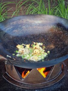 Mongolisches Rindfleisch mit Zwiebeln und grünen Erbsen in schwarz patiniertem Wok über offener Flamme