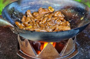 Mongolisches Rindfleisch mit Zwiebeln und Soße in der Wok-Pfanne über offener Flamme