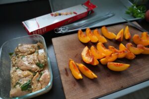 Marinierte Hähnchenbrustfilets in Schale und frische Pfirsichspalten auf Schneidebrett zur Vorbereitung von Hähnchen-Pfirsich-Spießen