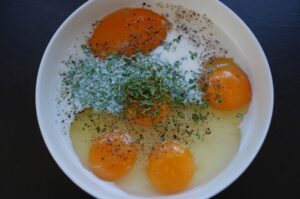 Rohe Eier in weißer Schüssel mit Kartoffeln, gehackter Petersilie und schwarzem Pfeffer für Bauernfrühstück aus der Heißluftfritteuse