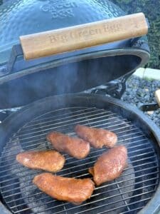 Fünf Hähnchenbrusthälften auf dem Grillrost eines Big Green Egg Keramikgrills während des Räuchervorgangs