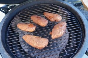Fünf Hähnchenbrusthälften auf dem Grillrost eines Kamado-Grills, leicht gebräunt mit Raucharoma