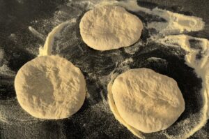 Frische Pizzateig-Rohlinge mit Mehl bestäubt auf dunkler Arbeitsfläche zur Vorbereitung der Pizza Fritta