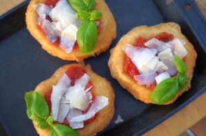 Drei Pizza Fritta mit Tomatensauce, Mozzarella-Würfeln, Schinken und frischen Basilikumblättern auf schwarzem Teller