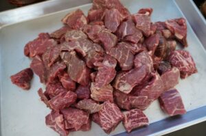 Rindfleisch-Würfel für Gulasch auf weißem Teller, in grobe Stücke geschnitten, Fleischfasern sichtbar