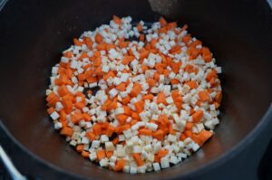 Gewürfelte Karotten und Zwiebeln in schwarzem Dutch Oven angerichtet, Zubereitungsschritt für Rindergulasch
