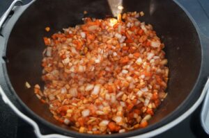 Gewürfelte Paprika und Zwiebeln werden in schwarzem Dutch Oven angebraten