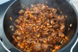 Rindergulasch mit Fleischwürfeln und Gemüsewürfeln in schwarzem Dutch Oven während des Garvorgangs
