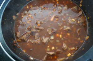 Rindergulasch mit Fleischstücken und Gemüse in braune Soße in schwarzem Dutch Oven
