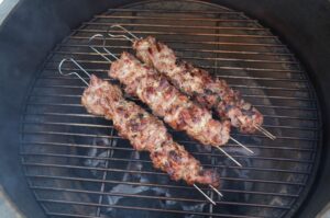 Fünf Spider-Steak-Spieße mit Fleischwürfeln auf dem Grillrost eines Kugelgrills, mit Röstmarks von der Hitze