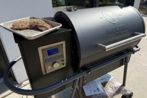 Tri-Tip-Burnt-Ends mit Gewürzmischung in Behälter auf Moesta BBQ Pelletgrill neben digitaler Steuereinheit