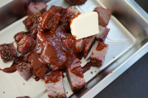 Tri-Tip-Burnt-Ends mit glänzender BBQ-Sauce und Butterwürfel auf weißem Tablett serviert
