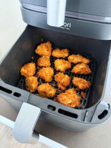 Goldbraun panierte Chicken Nuggets mit Cornflakes-Kruste in der schwarzen Behältnis einer Ori Air-Fryer-Maschine