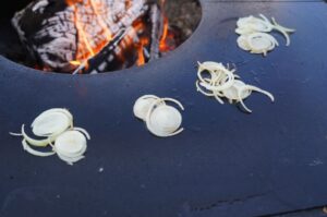 Geschnittene Zwiebeln auf heißer Grillplatte über offener Flamme, Zubereitung für Oklahoma-Style Smashburger