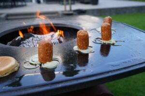 Gegrillte Smashburger-Pattys mit karamellisierten Zwiebeln auf Grillplatte über offener Flamme, dazu Brötchen, Donlicate-Rezept
