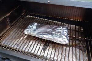 Aluminiumfolie-verpackte Spare Ribs auf dem Rost eines Gasgrill, Räuchern im indirekten Bereich