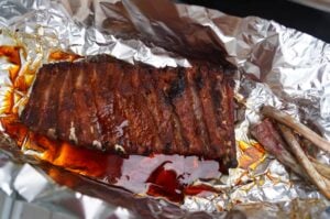 Gegrillte Spare Ribs mit karamellisierter Oberfläche auf Alufolie, daneben Barbecue-Sauce