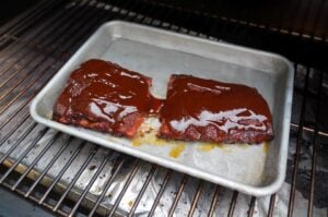 Zwei glasierte Spare Ribs auf Grill-Tablett, mit glänzender Barbecue-Sauce überzogen, während des Grillens