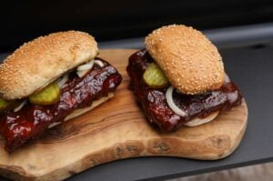 Zwei McRib-Sandwiches mit Sesambrötchen, gegrillten Spare Ribs, Barbecue-Sauce, eingelegten Gurken und Zwiebeln auf Holzbrett