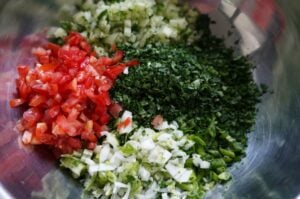 Geschnittene Zutaten für Tabouleh in einer Metallschüssel: gehackte Tomaten, frische Petersilie, fein geschnittene Zwiebel und grüne Zwiebeln