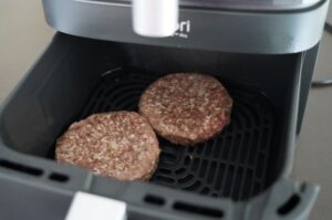 Zwei Beef-Patties in der Heißluftfritteuse während des Garvorgangs, auf schwarzem Gitterrost