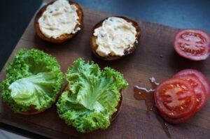 Toasted Burger-Brötchen mit Kräutercreme, Blattsalat und Tomatenscheiben auf Schneidebrett – Zubereitungsschritte für Air-Fryer-Burger