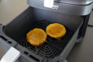 Zwei Hamburger-Patties mit gelblich-brauner Oberfläche in der Heißluftfriteuse während des Garvorgangs