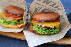 Zwei Burger aus der Heißluftfritteuse in Papierwickeln mit Cheddar-Käse, grünem Salatblatt und Tomatenscheiben auf Holzoberfläche