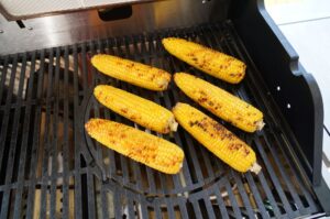 Sechs Maiskolben mit Grillmarkierungen auf Gasgrill-Rostelementen, Zubereitung für mexikanischen Maissalat Esquites