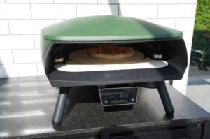 Pizza mit Pfifferlingen, Speck und Bergkäse auf Pizzastein in elektrischem Pizzaofen, Digital-Display zeigt 94°C