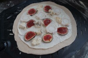 Flammkuchen mit Creme fraîche, halbierten frischen Feigen und Ziegenkäse auf schwarzem Grillblech