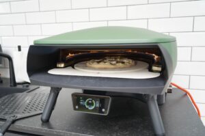 Feigenpizza mit Ziegenkäse und Serrano-Schinkel auf Pizzastein in grünem Elektro-Pizzaofen mit glühenden Infrarot-Heizelementen, Temperaturanzeige 443°C