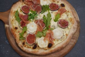 Feigenpizza mit Feigenscheiben, Prosciutto, Mozzarella, Rucola auf Holzbrett serviert