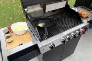 Grill mit Mise-en-place für Nackensteaks mit Miso-Zwiebeln: Schüssel mit gehackten Zwiebeln, Dosen mit Miso-Paste und Zucker auf Schneidebrett, schwarze Grillpfanne mit Butter auf Grillrost