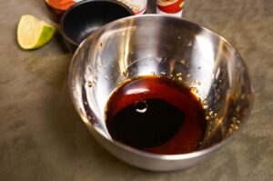 Braune Soßenmischung aus Fischsoße, Sojasauce und Palmzucker in einer Metallschüssel, daneben Limettenstück