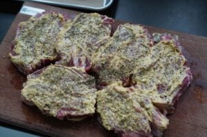 Fünf Thüringer Rostbrätel mit Gewürzen auf Holzbrett, vor dem Grillen