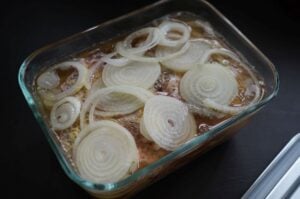 Thüringer Rostbrätel mit Zwiebeln in Glasauflaufform, mariniert mit Sauce und frischen Zwiebelringen, vor dem Grillen