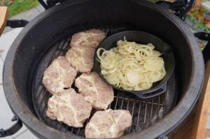 Thüringer Rostbrätels auf Grillrost mit Zwiebeln in Pfanne im Kugelgrill