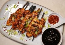 Yakitori-Spieße mit glasiertem Hähnchenfleisch, Sesam, grünem Frühlingszwiebel-Topping und Chilliflocken. Dazu Schälchen mit Sojasauce und Chili-Öl.