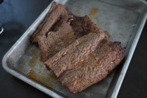 Gegrillte Döner-Fleischstücke auf Backpapier in Aluminiumbehälter, medium-rare Garstufe mit Grillmarks