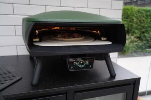 Salsiccia-Pizza mit Ziegenkäse und roten Zwiebeln im grünen Elektro-Pizzaofen mit digitaler Temperaturanzeige