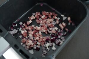 Gewürfelte Speckstücke und Zwiebelwürfel in schwarzem Grillbehälter