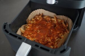 Schupfnudeln-Flammkuchen in der Heißluftfritteuse goldbraun ausgebacken, auf Backpapier in schwarzem Frittierkorb