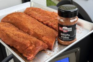 Cadillac Cut Spare Ribs mit BBQPit Pork Rub auf weißem Blech, daneben Gewürzdose mit Würzmischung